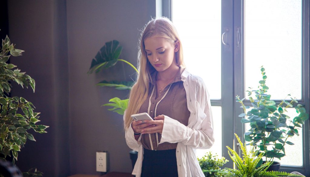 Woman holding a phone, browsing social media, highlighting the need for caution when sharing personal details online.