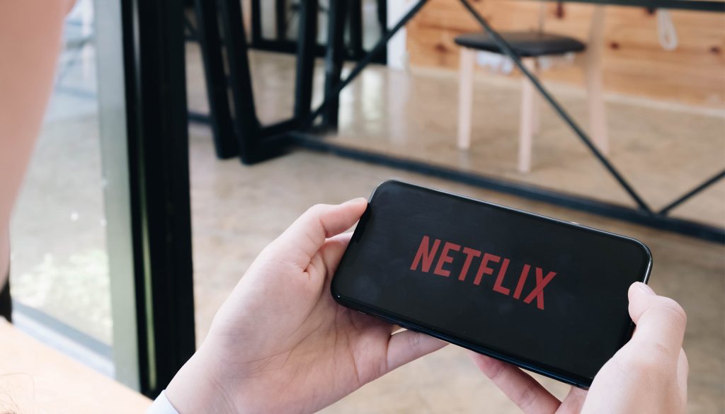 Photo of a person holding a phone displaying the netflix logo.