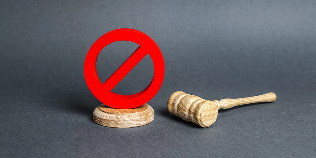 A red prohibition symbol next to a wooden gavel, representing legal restrictions and internet censorship laws.