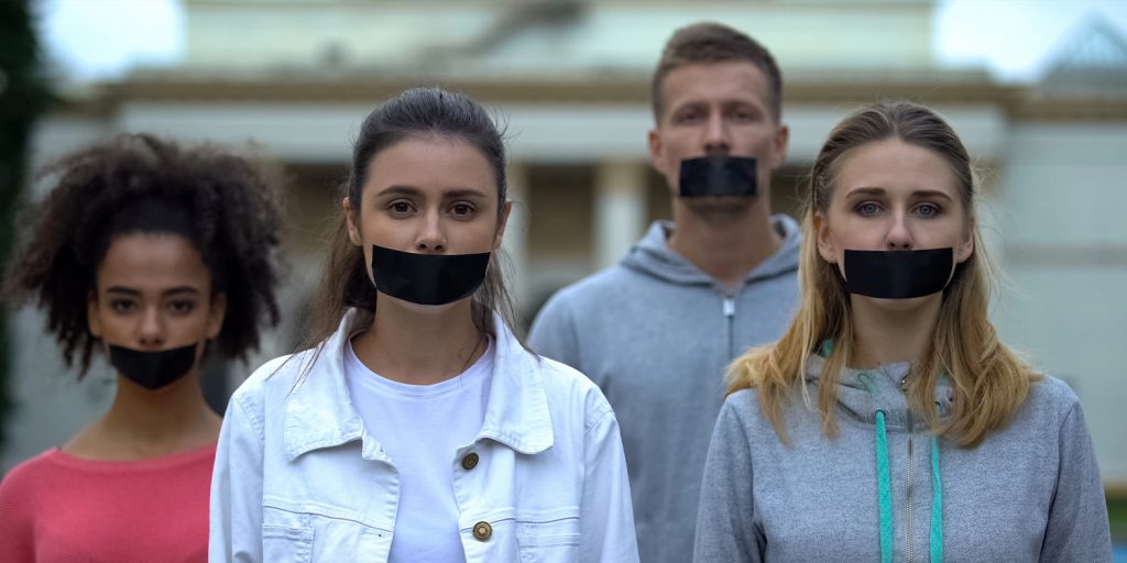 Four people standing with black tape over their mouths, symbolizing censorship and silenced voices.