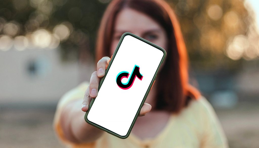 Woman holding a smartphone displaying the TikTok logo prominently on the screen.